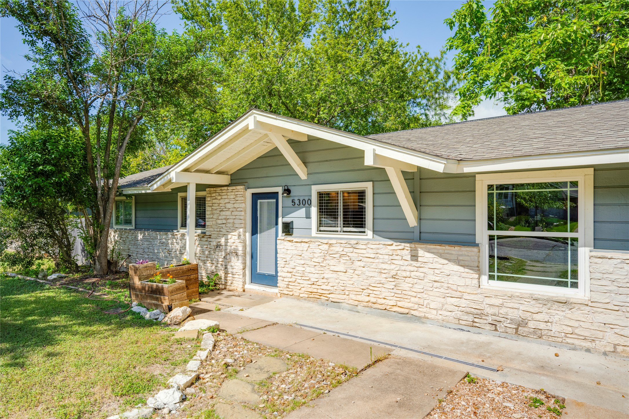 5300 Halmark Drive Austin, TX 78723 - Photo 2 of 40 A welcoming facade showcases stone accents and a vibrant blue entry door, blending natural elements with modern appeal.