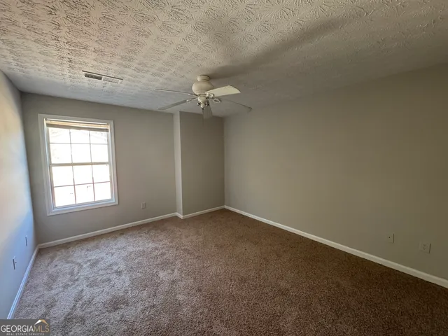 an empty room with chandelier fan and windows
