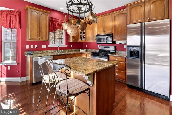 a kitchen with stainless steel appliances granite countertop a kitchen island a stove a refrigerator a dining table and chairs with wooden floor