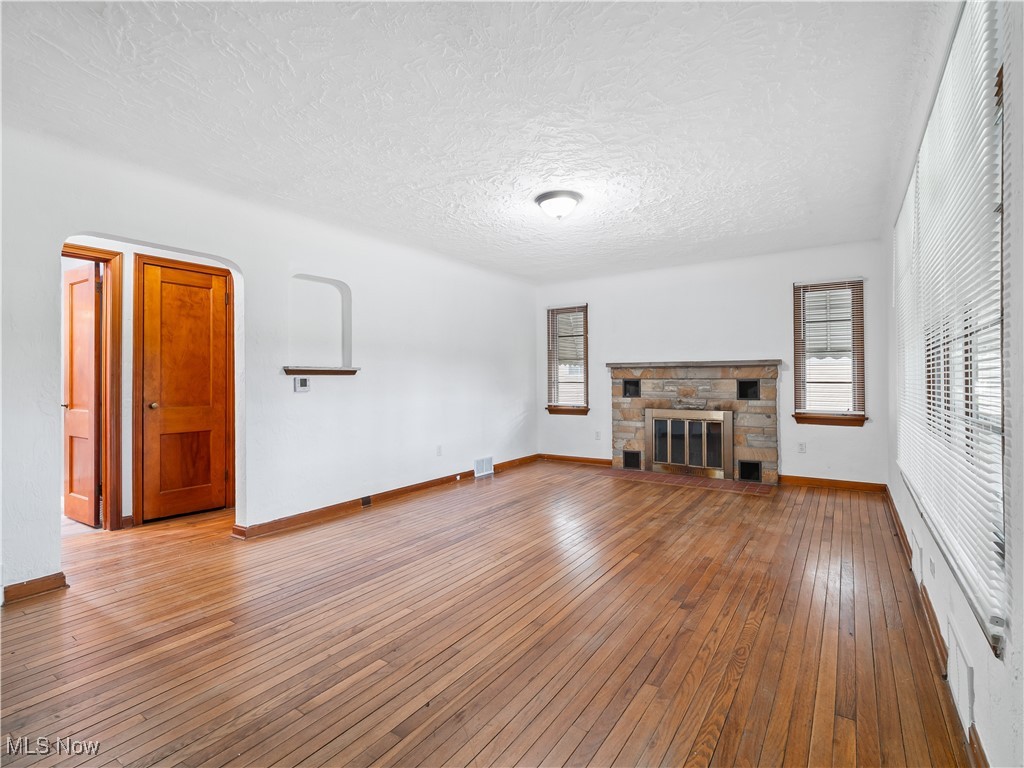 3605 Center Road Avon, OH 44011 - Photo 7 of 34 Unfurnished living room featuring light hardwood / wood-style flooring, a textured ceiling, and a stone fireplace