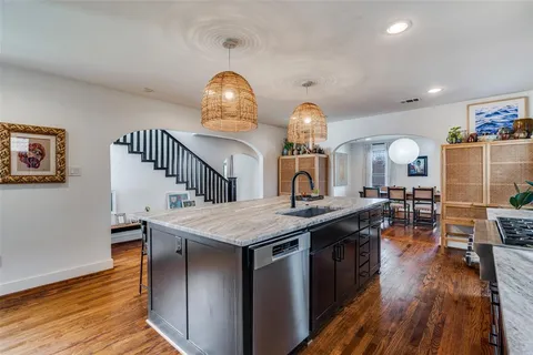 a kitchen with stainless steel appliances granite countertop a sink dishwasher a stove and a dining table with wooden floor