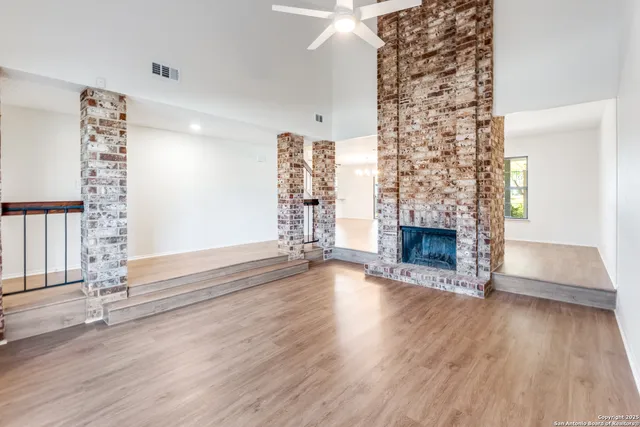 an empty room with wooden floor chandelier fan and windows