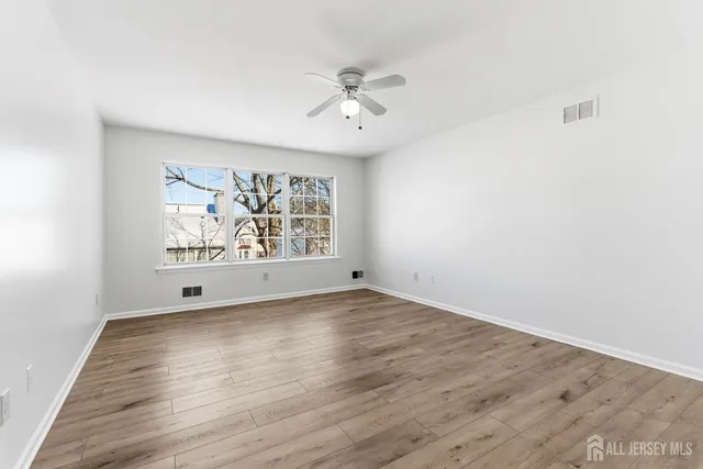 an empty room with wooden floor ceiling fan and windows