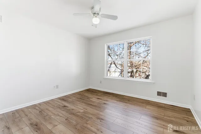 an empty room with wooden floor chandelier fan and windows