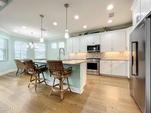 a kitchen with stainless steel appliances granite countertop a refrigerator oven a sink dishwasher a dining table and chairs with wooden floor