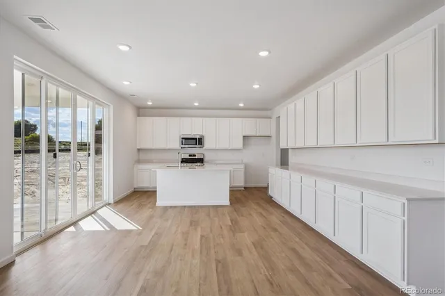 a large kitchen with stainless steel appliances a large counter top a stove and a wooden floors