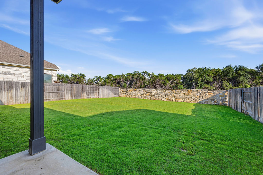 2032 Base Burner Path Leander, TX 78641 - Photo 34 of 34 Spacious backyard featuring an expansive lawn, a stone retaining wall, and a wood privacy fence