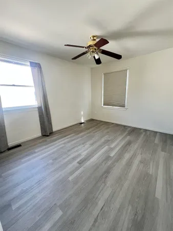 an empty room with wooden floor a ceiling fan and windows