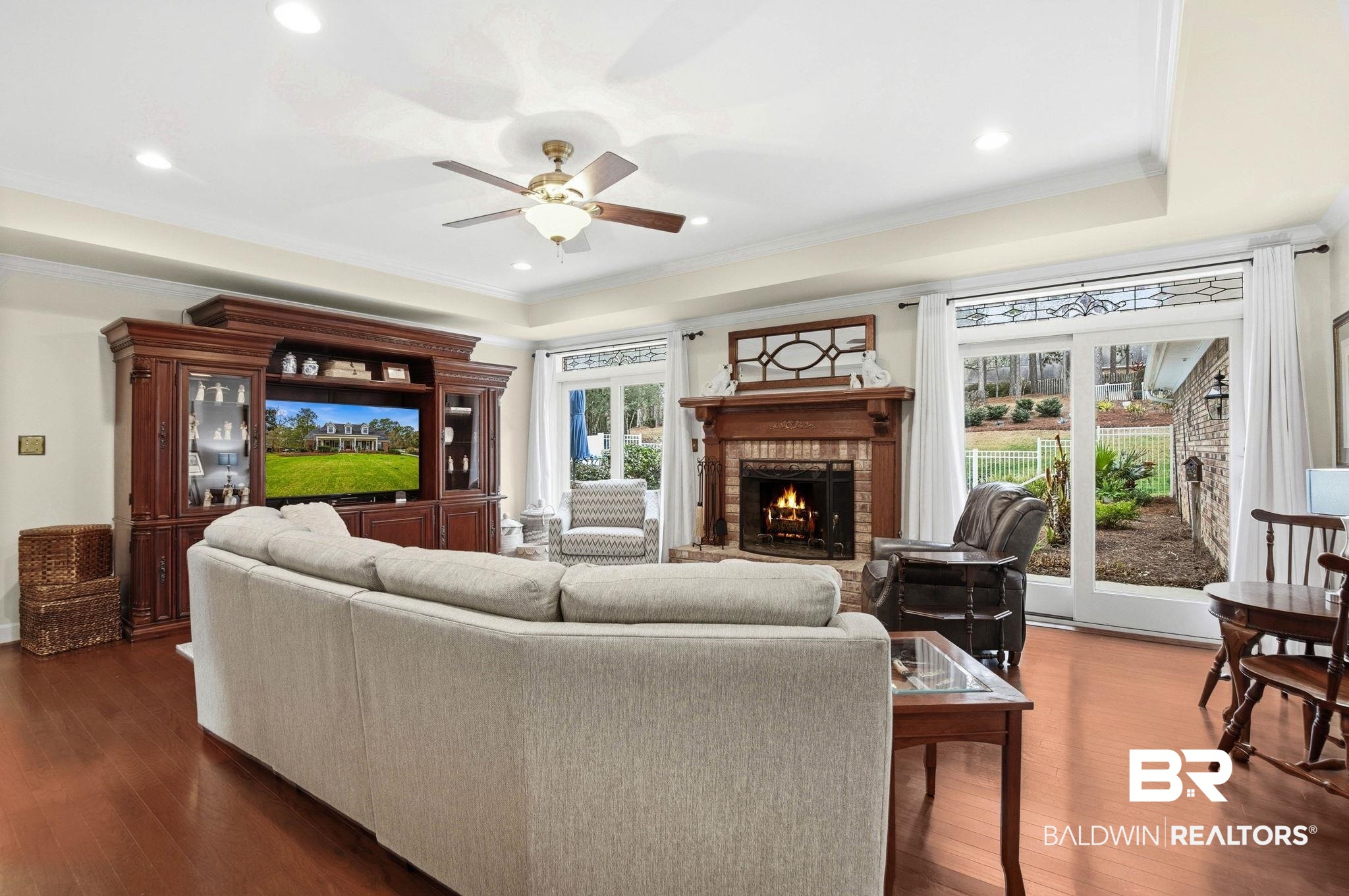 31515 Rhett Drive Spanish Fort, AL 36527 - Photo 24 of 100 The Great Room measures 21' 7' x 17' 7' and has beautiful engineered hardwood floors, crown molding, tray ceilings, two Andersen sliding doors (2024) with lead glass decorative transom to the patio and pool area, and a woodburning fireplace.