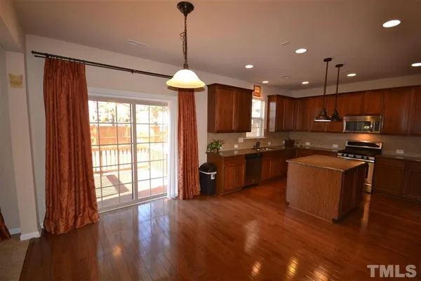 a kitchen with stainless steel appliances granite countertop wooden cabinets a refrigerator a sink a stove and a wooden floors