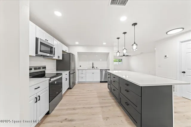 a large kitchen with stainless steel appliances kitchen island granite countertop a stove a sink dishwasher and a refrigerator with wooden floor