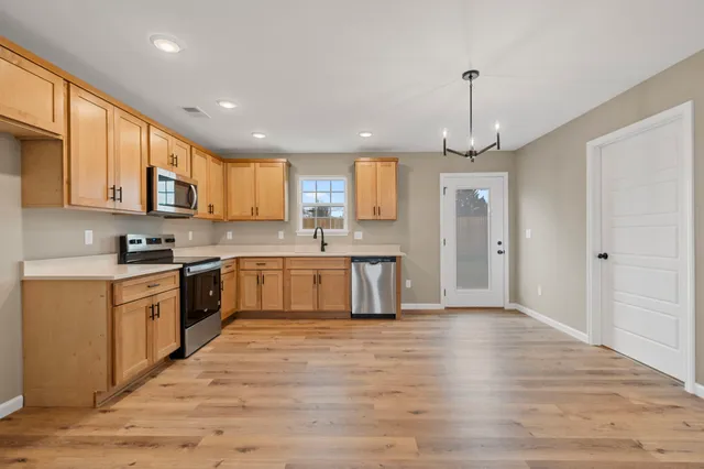 a large kitchen with stainless steel appliances granite countertop a stove a sink dishwasher a refrigerator white cabinets and wooden floor