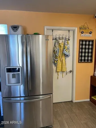 a view of a refrigerator in kitchen and an empty room with wooden floor