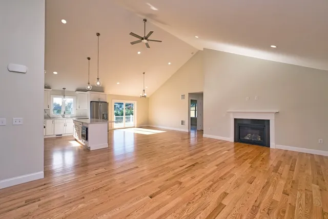 a view of an empty room and kitchen with fireplace wooden floor