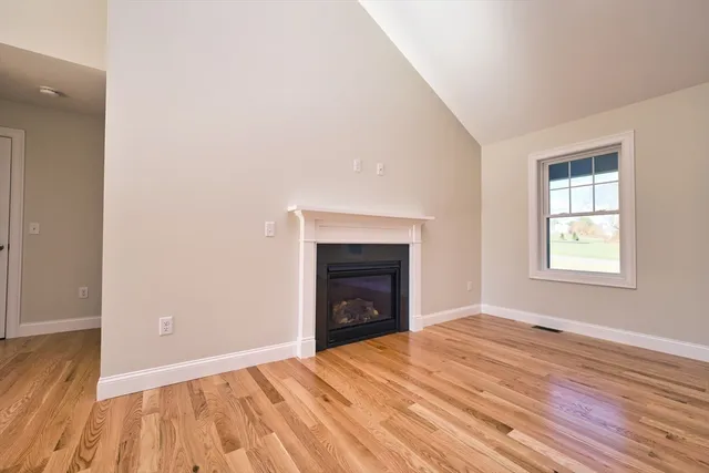 a view of an empty room with wooden floor fireplace and a window