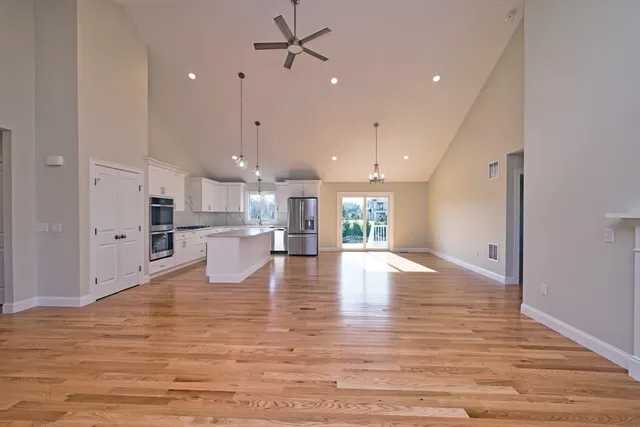 a view of a kitchen with kitchen island a refrigerator a sink dishwasher a oven and a dining table with wooden floor