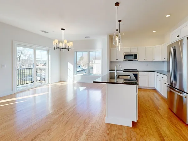 a large kitchen with stainless steel appliances granite countertop a stove a sink dishwasher a refrigerator white cabinets wooden floor and a fireplace