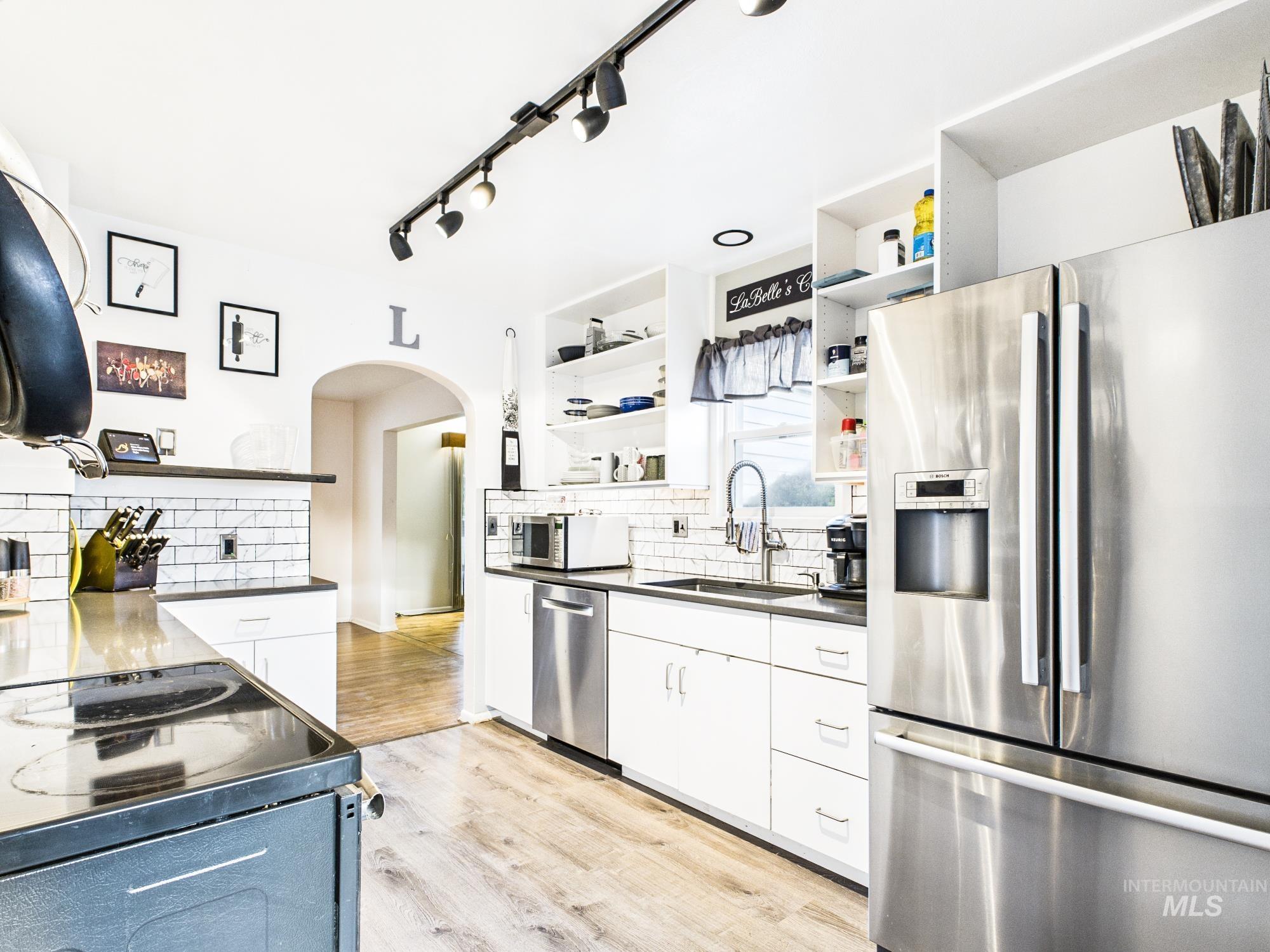 3422 6th Street Lewiston, ID 83501 - Photo 12 of 43 Modern kitchen featuring stainless steel appliances, white cabinetry, dark countertops, a subway tile backsplash, and wood-finish flooring
