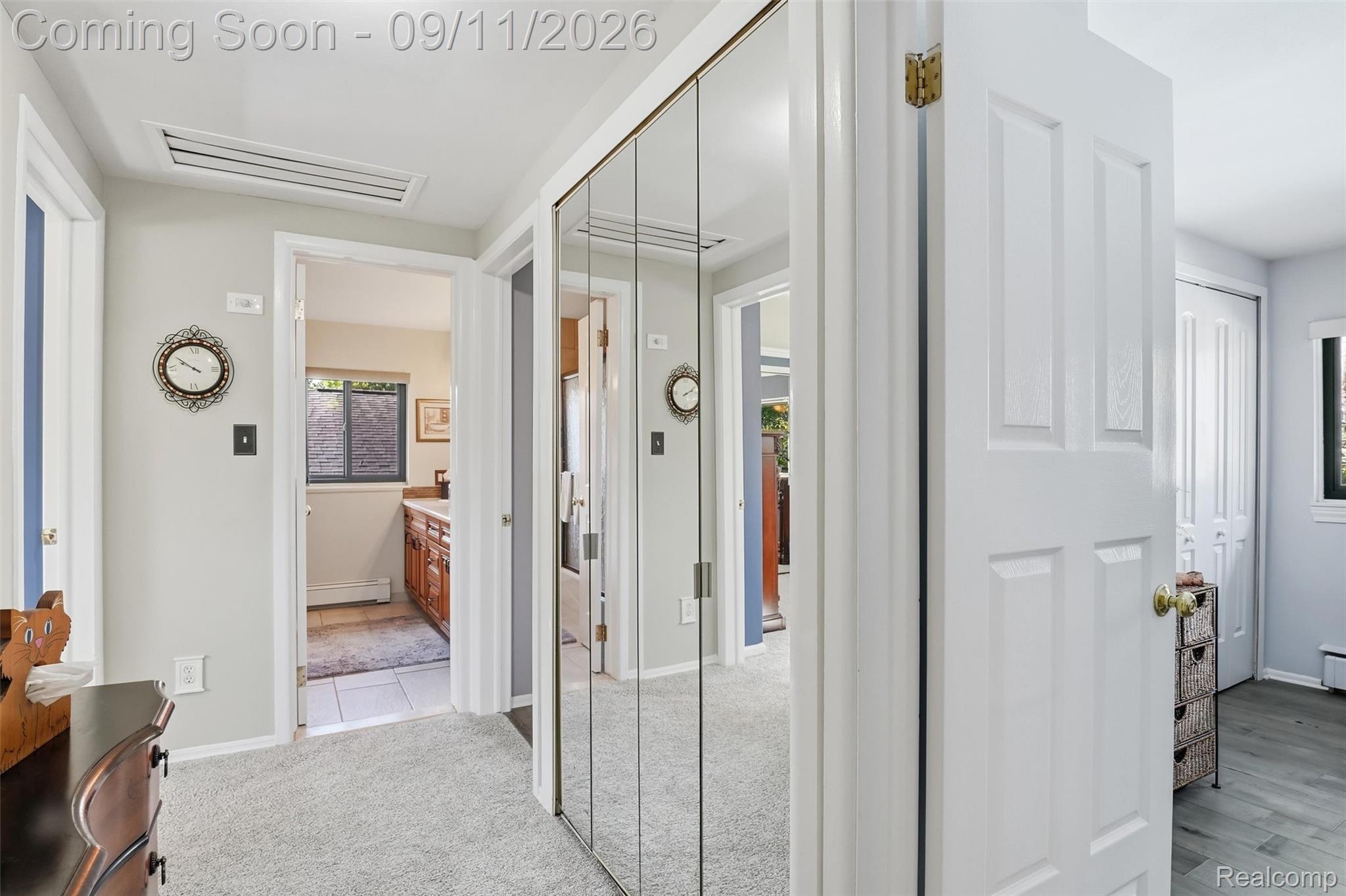 16799 Farmington Road Livonia, MI 48154 - Photo 22 of 71 Light gray wall finishes, light gray carpeting, mirrored closet doors, a white paneled door, and wood-finish flooring