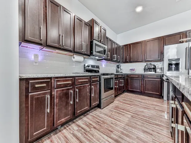 a kitchen with stainless steel appliances granite countertop wooden cabinets a stove top oven a sink and dishwasher with wooden floor