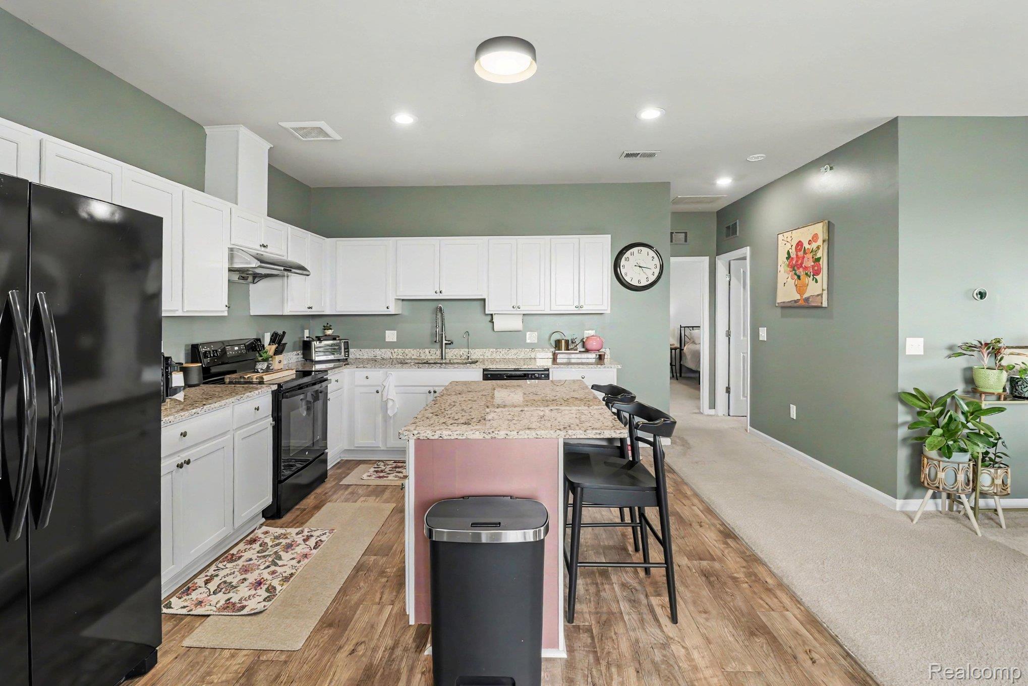 9864 Ridge Run Street Howell, MI 48855 - Photo 10 of 23 Kitchen featuring black appliances, a kitchen island, white cabinetry, light wood-style flooring, and a breakfast bar area