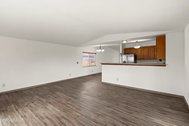 an empty room with wooden floor and kitchen view
