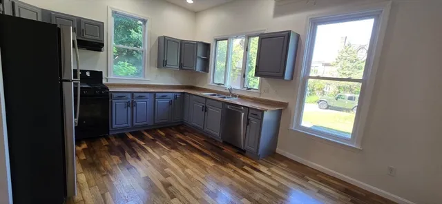 a kitchen with stainless steel appliances granite countertop a refrigerator a sink dishwasher a stove and white countertops with wooden floor