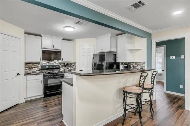 a kitchen with stainless steel appliances granite countertop a stove top oven a sink dishwasher a refrigerator and white cabinets with wooden floor