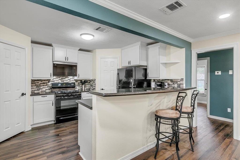 a kitchen with stainless steel appliances granite countertop a stove top oven a sink dishwasher a refrigerator and white cabinets with wooden floor