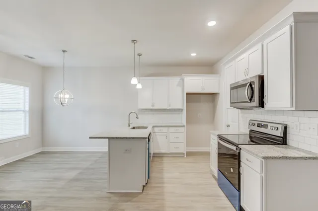 a kitchen with stainless steel appliances granite countertop a sink a stove and white cabinets with wooden floor