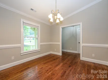an empty room with wooden floor chandelier and windows