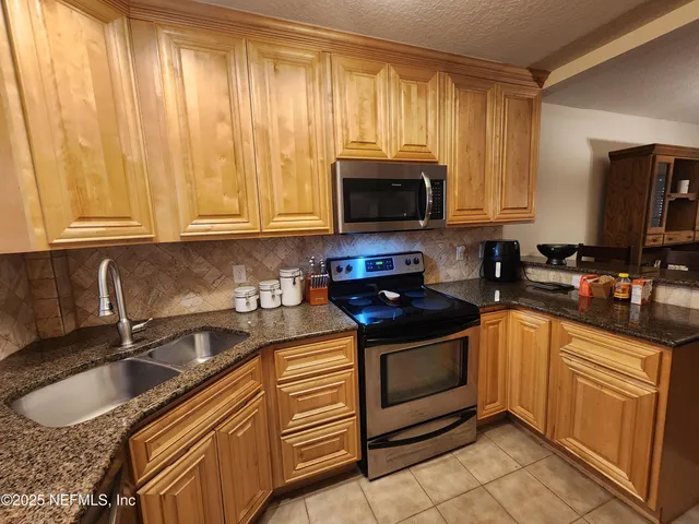 a kitchen with granite countertop a sink a stove top oven and cabinetry