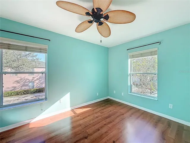 an empty room with wooden floor fan and windows