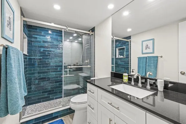 a bathroom with a granite countertop sink a toilet a mirror and shower