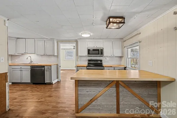a kitchen with kitchen island granite countertop a stove top oven a sink dishwasher a refrigerator and a cabinets with wooden floor