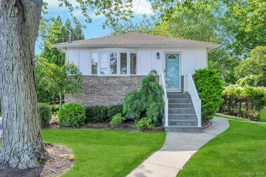 View of front of house with a shingled roof, a front lawn, and stone siding