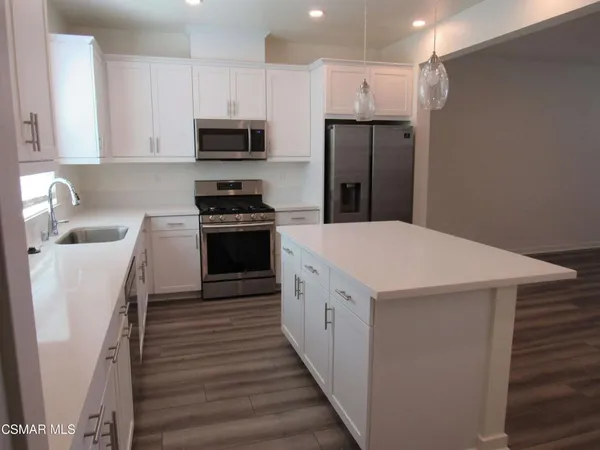 a kitchen with stainless steel appliances granite countertop a sink a stove a refrigerator and island with wooden floor