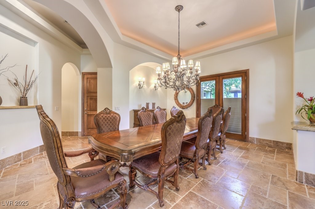 2780 El Camino Road Las Vegas, NV 89146 - Photo 29 of 91 Dining room featuring a chandelier, a tray ceiling, stone tile floors, and arched walkways