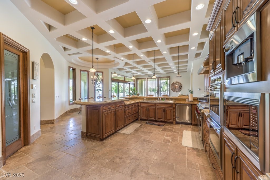 2780 El Camino Road Las Vegas, NV 89146 - Photo 36 of 91 Kitchen with coffered ceiling, brown cabinetry, stone tile floors, decorative light fixtures, and dark stone counters