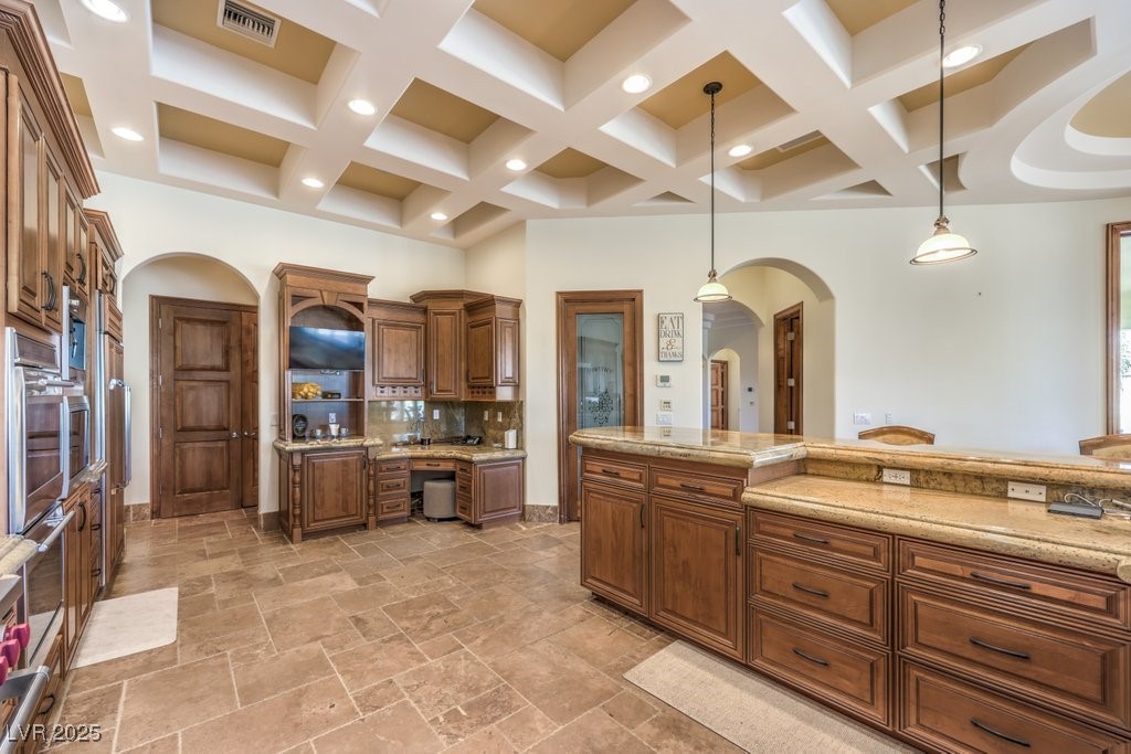 2780 El Camino Road Las Vegas, NV 89146 - Photo 37 of 91 Kitchen with arched walkways, brown cabinetry, pendant lighting, backsplash, and coffered ceiling