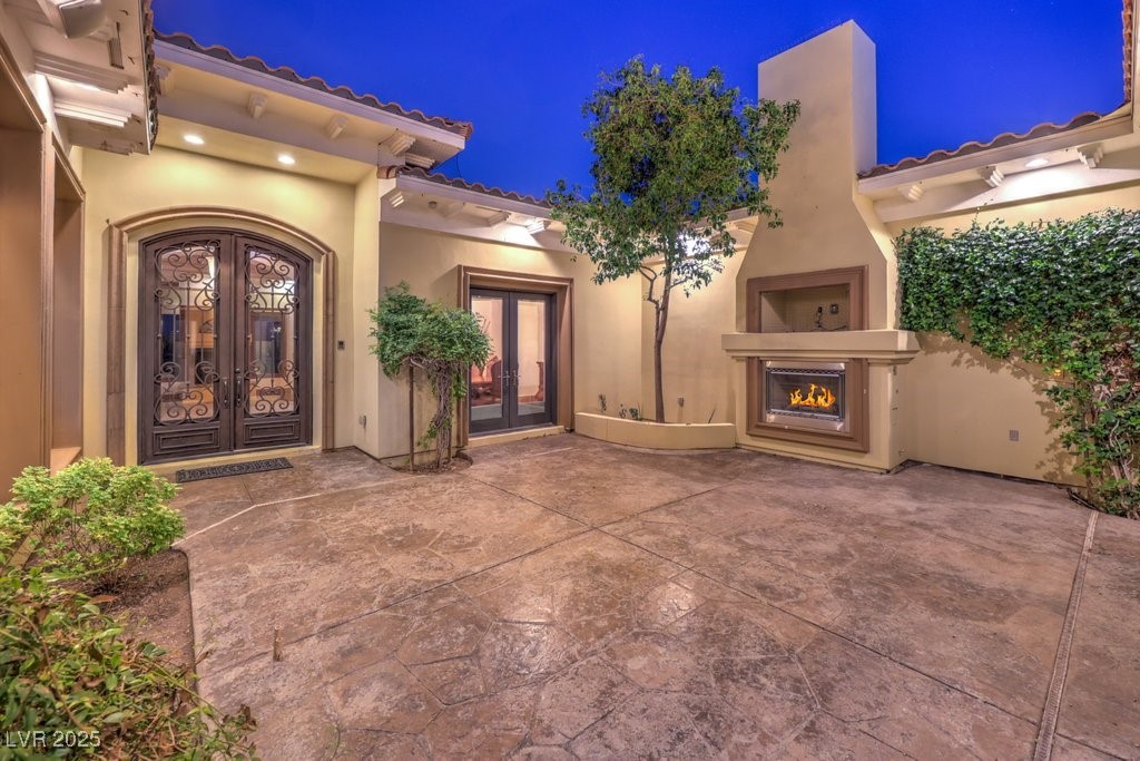 2780 El Camino Road Las Vegas, NV 89146 - Photo 7 of 91 Exterior entry at night with french doors, a lit fireplace, stucco siding, and a tile roof