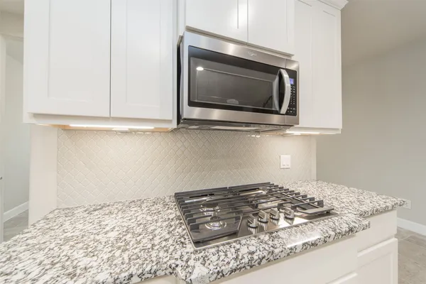 a kitchen stove with granite countertop white cabinets and a stove