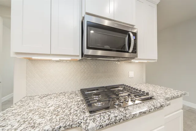a kitchen stove with granite countertop white cabinets and a stove