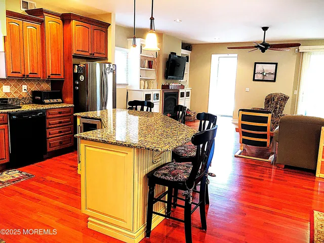 a kitchen with stainless steel appliances granite countertop a refrigerator a stove top oven a dining table and chairs with wooden floor