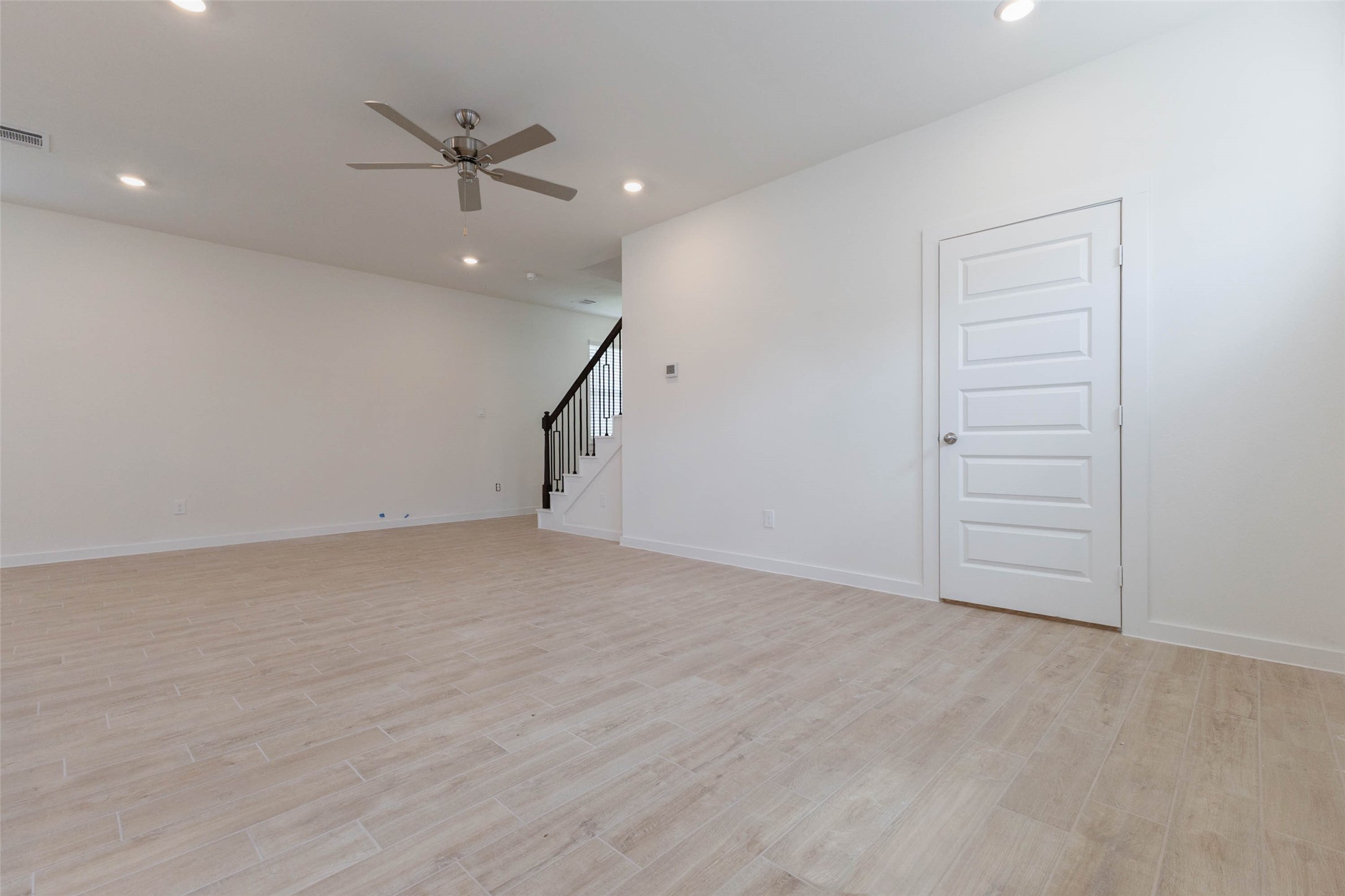 1115 Santee Court Rosharon, TX 77583 - Photo 12 of 23 Another angle of the main living space shows a ceiling fan, a closet door for coat or cleaning storage and the staircase tucked in the corner. The wood-look floors are easy to clean and sturdy for kids and pets, and the neutral walls pair with any decor. There is plenty of space to define a seating area and a dining area without feeling crowded.