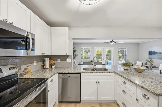 a kitchen with granite countertop a sink dishwasher stove and white cabinets with wooden floor
