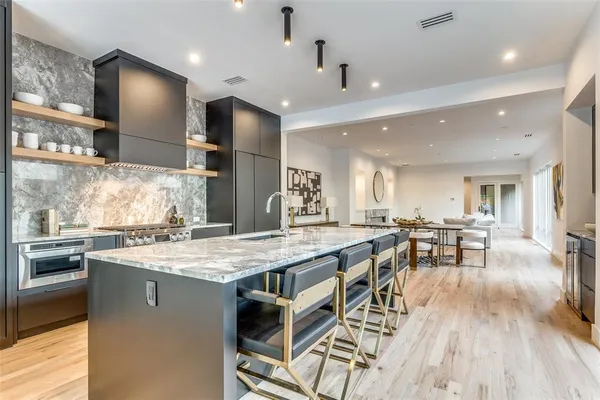 a kitchen with stainless steel appliances granite countertop a stove a refrigerator a kitchen island a dining table and chairs with wooden floor