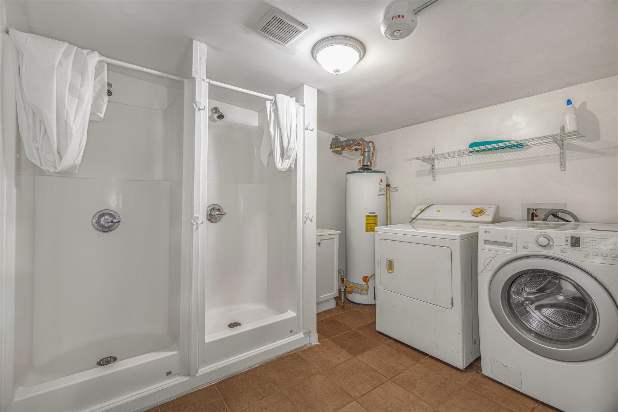 905 43rd Street Galveston, TX 77550 - Photo 22 of 43 This room features a laundry area with a washer and dryer, a hot water heater, and two shower stalls. It has tiled flooring, a ceiling light, and a wall-mounted shelf for storage.