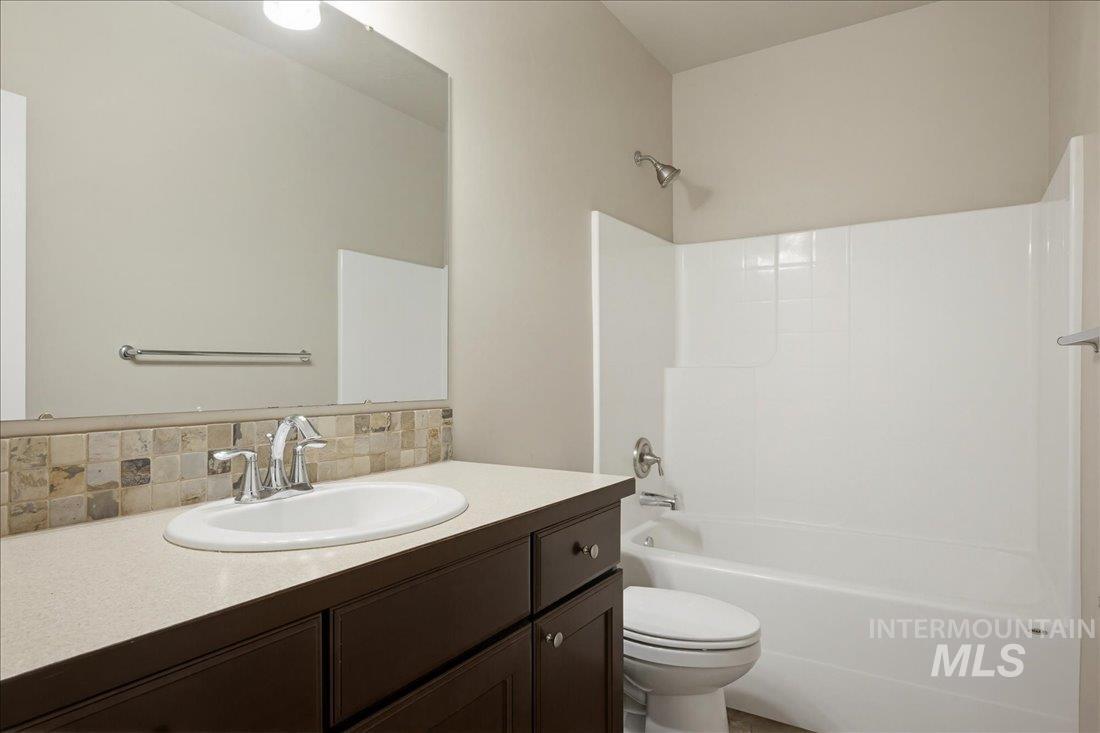 12460 West Azure Street Boise, ID 83713 - Photo 29 of 34 Bathroom featuring an integrated bathtub and shower with white surround, a toilet, and a vanity with a light-toned countertop, an undermount sink, and a tiled backsplash