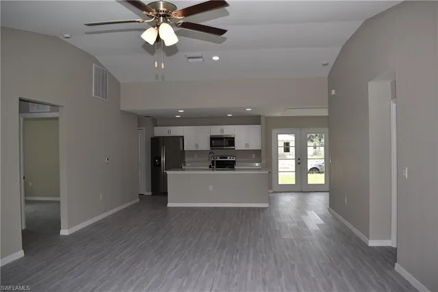 a view of a kitchen and an empty room with wooden floor and a window